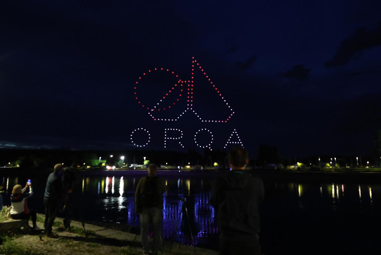 Drone formation spelling 'ORQA' with a logo above a waterfront crowd